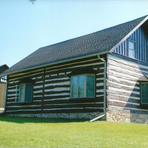 Rustic log cabin with green shutters finished in Tobacco